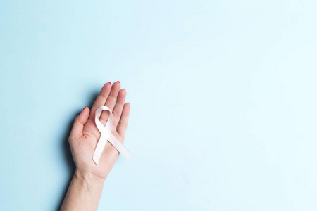 Female hand holding white ribbon on a blue background. 