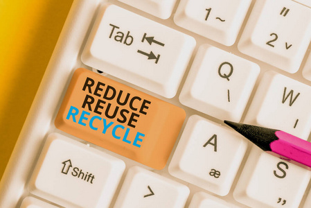 文字标志显示减少再利用回收。概念照片环境对消费者行为负责白色电脑键盘，白色背景键上方有空白便笺。