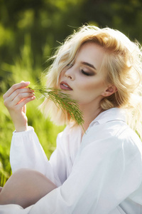 Girl in a long white dress sits on the grass in a field. Blonde 