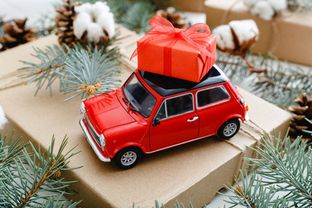 车顶有圣诞红礼盒的红色玩具车.圣诞背景为棉花,冷杉树枝,冷杉球果.