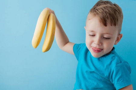 小男孩拿着一个蓝色背景的香蕉吃着，食物