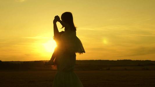 一个小女孩坐在妈妈的肩膀上,在阳光下一起在公园里散步,面带微笑.