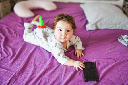 儿童和移动设备。小女孩躺在床上看着智能手机