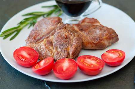 香喷喷的猪肉牛排，加香料西红柿和酱汁，放在灰色盘子上，深色混凝土背景上，有文字位置