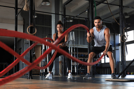 运动型年轻夫妇与战斗绳在功能训练健身馆锻炼。