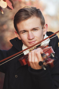 秋日自然背景下，一位年轻优雅的男子拉小提琴，一个男孩带着弓乐器练习，户外音乐表演，爱好和艺术观念