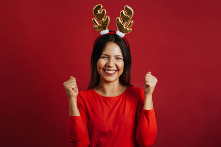 快乐的女人戴着圣诞驯鹿角头巾在红色背景上庆祝