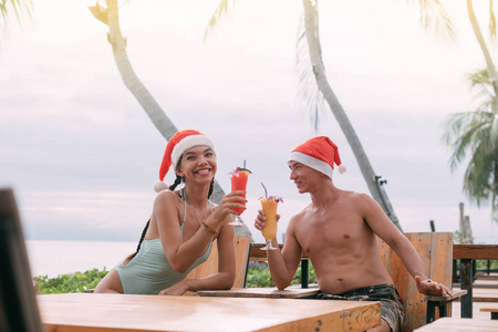 Young couple with cocktails in Christmas caps on the ocean on a 