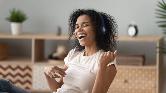 快乐的美国黑人妇女戴着耳机听音乐,唱歌照片