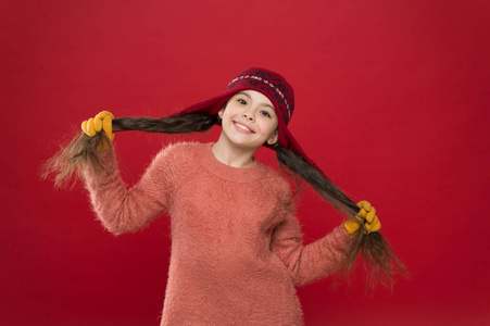 波浪发型是本季的冠军。快乐的女孩抱着深色头发的红色背景。小孩子把帽子戴在长发上。凉爽的冬季发型。尝试新的造型和发型
