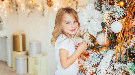 圣诞夜在家里装饰圣诞树的小女孩。小朋友在有冬季装饰的灯光房里。家庭幸福。新年12月庆祝时间概念横幅