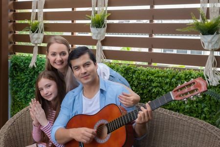 father play guitar or music with daughter and mother sitting on 