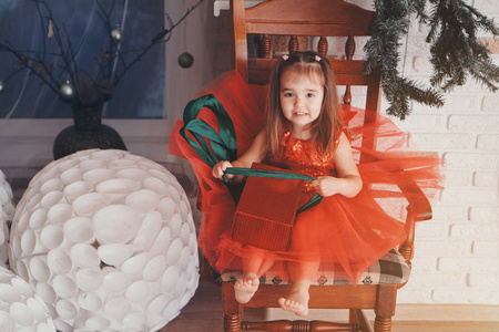 穿红衣服的小女孩打开新年礼物。庆祝圣诞节午夜的概念