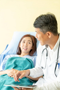 Asian senior doctor sitting on hospital bed and discussing with 