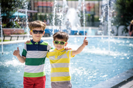 一群快乐的孩子在室外游泳池或喷泉旁玩耍。暑假期间，孩子们在公园里拥抱大拇指。穿着五颜六色的t恤和短裤，戴着墨镜。暑假康赛