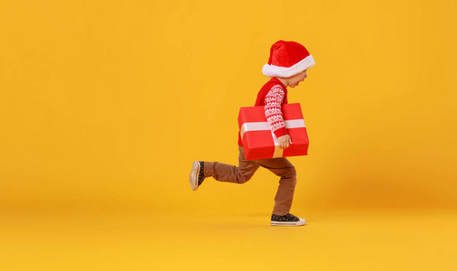 快乐有趣的红衣小男孩带着圣诞礼物跑步