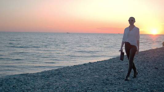 夕阳下,年轻美丽的光头女孩走在海滩上.