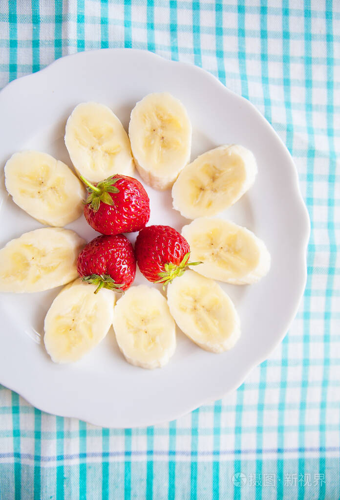 香蕉和草莓放在白色盘子和一张彩色餐巾上