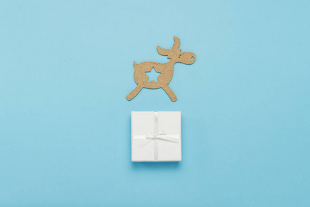 蓝色背景上的木制圣诞玩具鹿和白色礼品盒