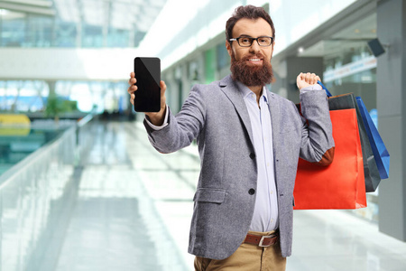 Man with shopping bags in a mall showing a mobile phone 