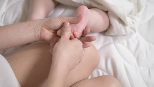 女性在床上用手按摩婴儿。特写镜头