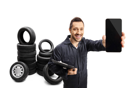 Auto mechanic showing a mobile phone with car tires in the back 