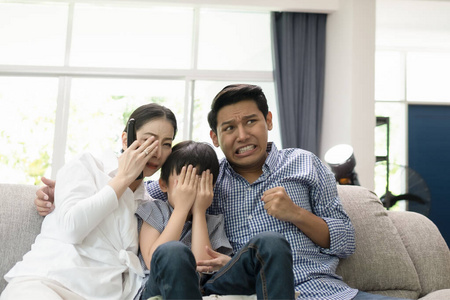 young family, father, mother and son watching TV feeling scared 