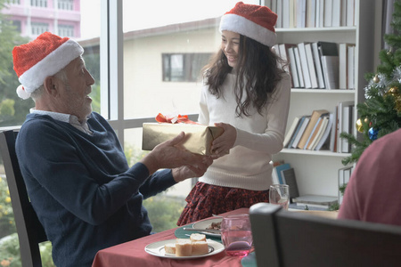 little girl giving a present or gift to senior man wear red hat 