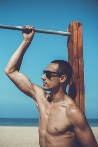 年轻肌肉男在海滩上休息和摆姿势。戴墨镜