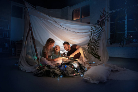 一家人坐在帐篷里，拿着手电筒读故事