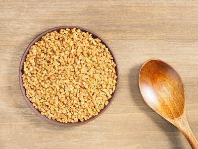 Fenugreek in clay plate on a brown wooden background and spoon. 