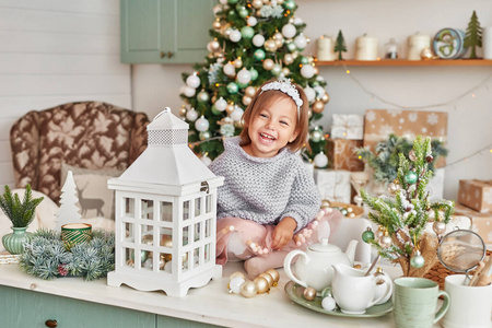 厨房里的女婴圣诞节。孩子看着相机微笑着。背景装饰冷杉树。厨房里的圣诞节。绿松石新年厨房装饰明亮厨房内部