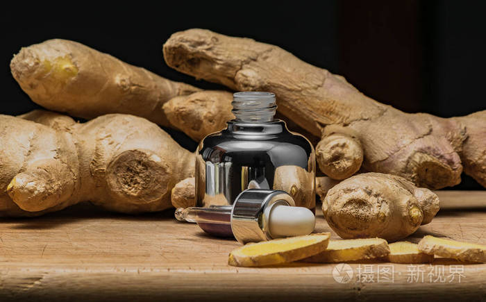 一瓶化妆品用玻璃吸管姜油提取物放在木板上用姜根黑色背景复印空间