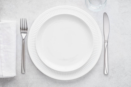餐桌摆设有白色盘子玻璃餐巾叉子和刀。