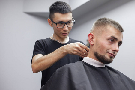 乌兹别克理发师在理发店给年轻帅哥理发,男顾客坐在美容院剪短发照片
