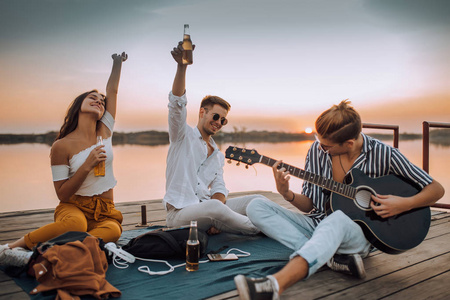 Happy friends playing the guitar and having fun on the beach in 