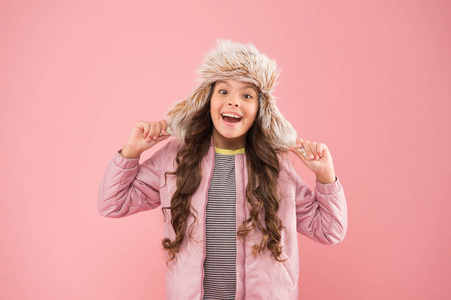 温暖的微笑。快乐儿童粉色背景。寒冷季节的保暖衣服。儿童时尚。时髦的女孩看起来很时髦。秋季风格。童年活动。毛皮耳垂帽配件。小女孩冬