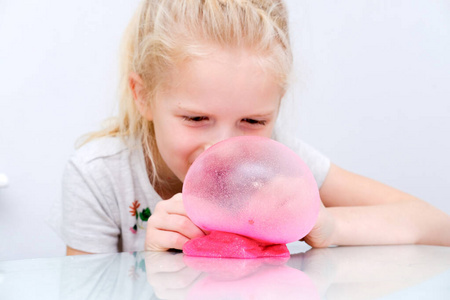 金发女孩用粉色闪光的粘液吹泡泡.玩黏液玩具.在家做黏液照片