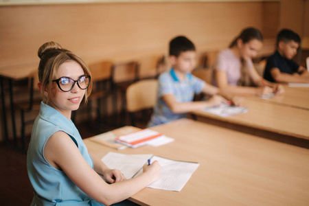 坐在黑板前教室里漂亮的老师坐在课桌前问孩子们.