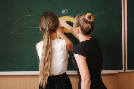 老师帮助黑板旁的女孩。青年女教师学习