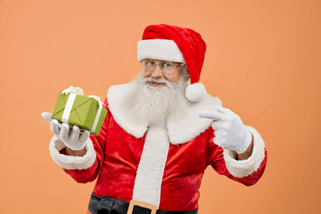 老圣诞老人看着相机，指着礼品盒
