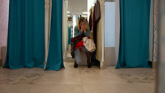 Girl sits in the fitting room with a bunch of clothes 