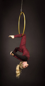 一个苗条的金发女孩一个穿着红色西装留着长发的空中杂技演员，在一个空气环里进行练习。