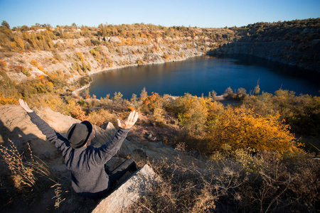 穿着毛衣,戴着黑帽子的自由人在夕阳下张开双臂欣赏秋湖的自然景色.