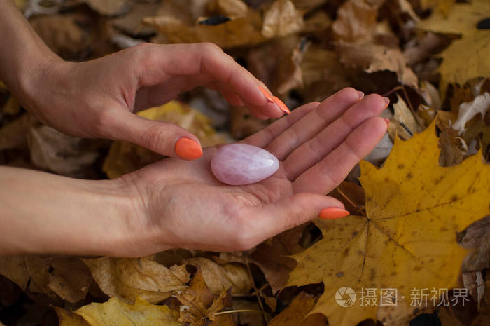 在秋天的户外橙色指甲的女性手拿着粉红色的石英yoni鸡蛋在黄色的落叶