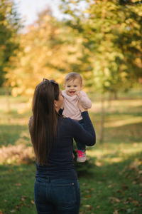 公园里美丽家庭的肖像。妈妈和女儿在秋天聚在一起。妈妈手上的十个月宝宝