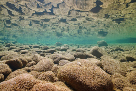 水面反射的水下岩石河床照片