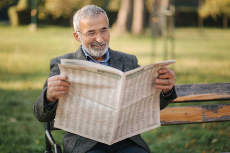 在秋天的公园里,戴着眼镜的大胡子老人在看报纸