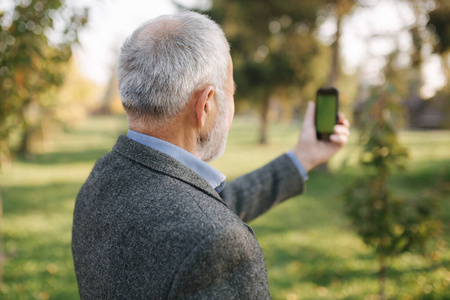 模拟老人在外面打电话。绿色屏幕。手持手机的男子的后视图