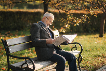 戴眼镜的白发老人在秋天的公园里,戴着眼镜的大胡子老人在看报纸